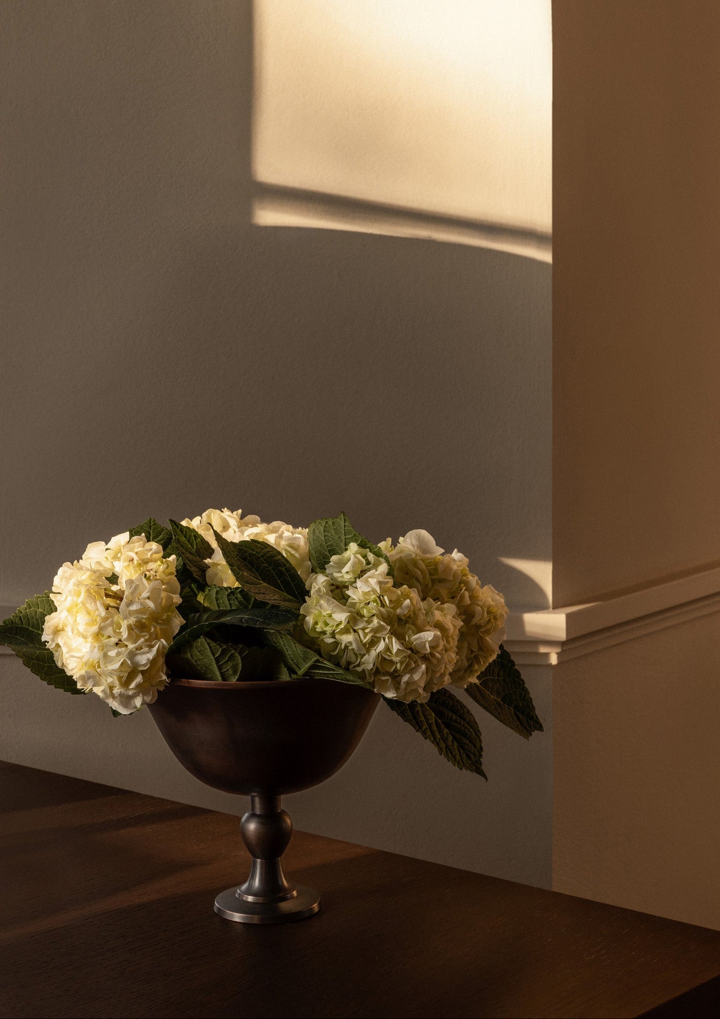 Decorative flower arrangement in a dark vase on a wooden surface with a neutral background
